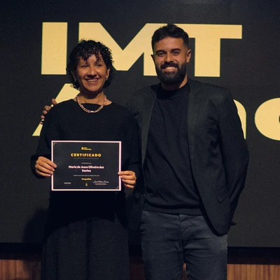 Maria de Jesus Oliveira dos Santos segura o certificado do Curso Cinegrafista ao lado de Israel Meira, na formatura de 09/09/2026